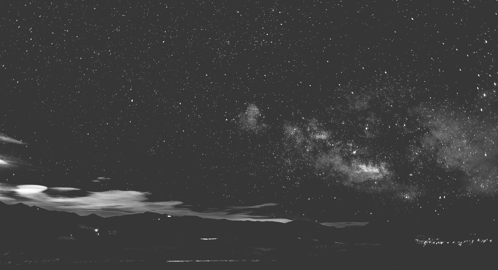 Starry night sky with the Milky Way and thin clouds over a dark horizon
