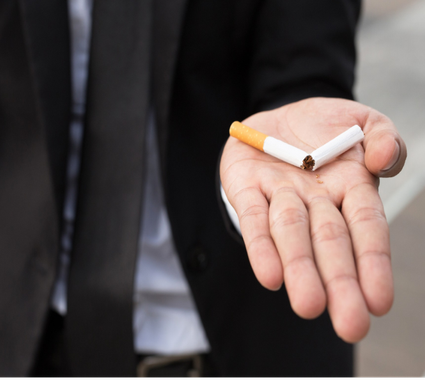Hand holding a lit cigarette, with a suit jacket in the background
