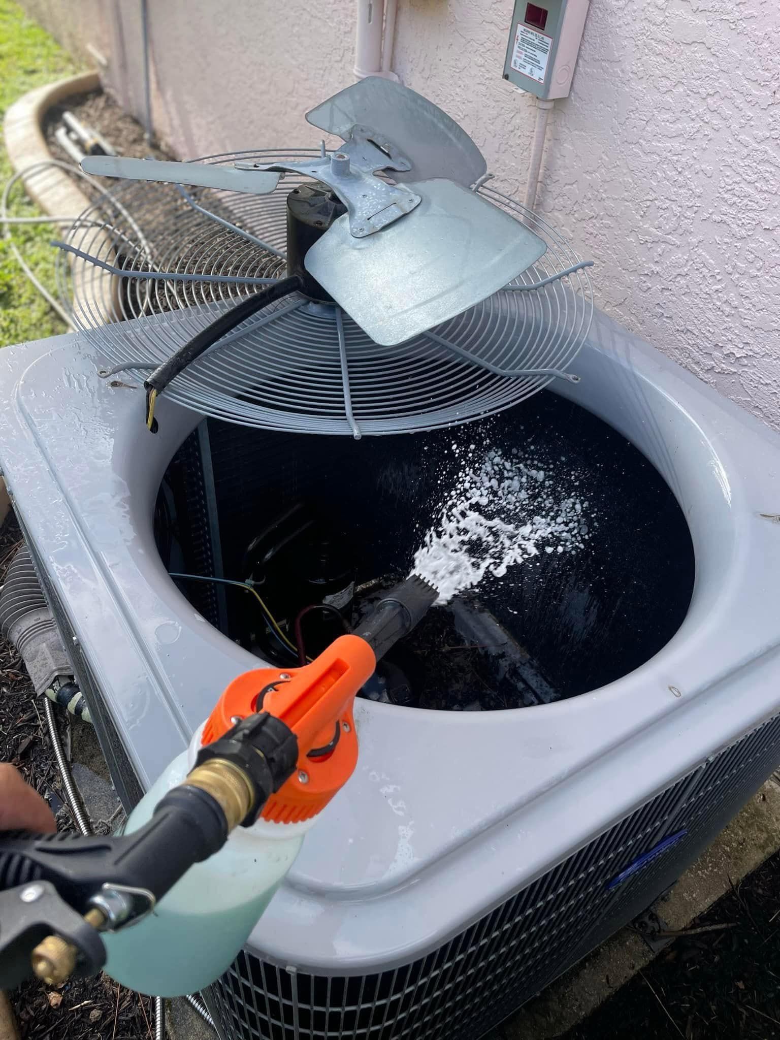 A Local Guy technician is cleaning an air conditioner with a hose.