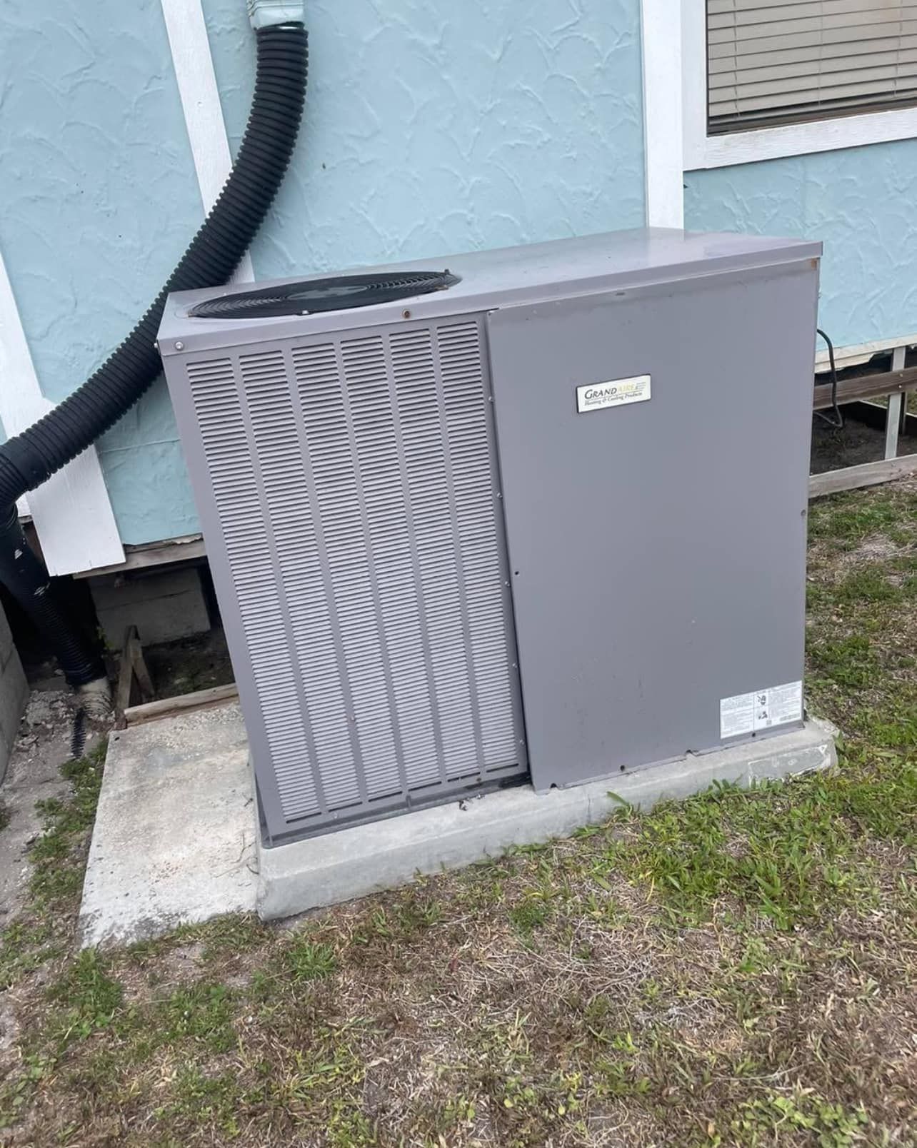 A gray air conditioner is sitting on the side of a building.
