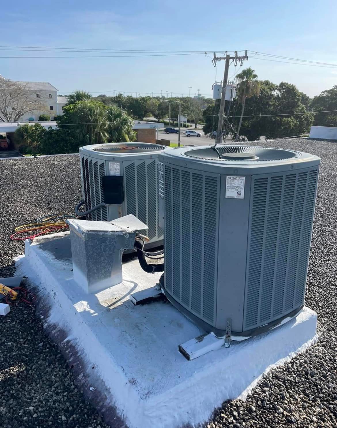 Two air conditioners are sitting on top of a gravel roof.