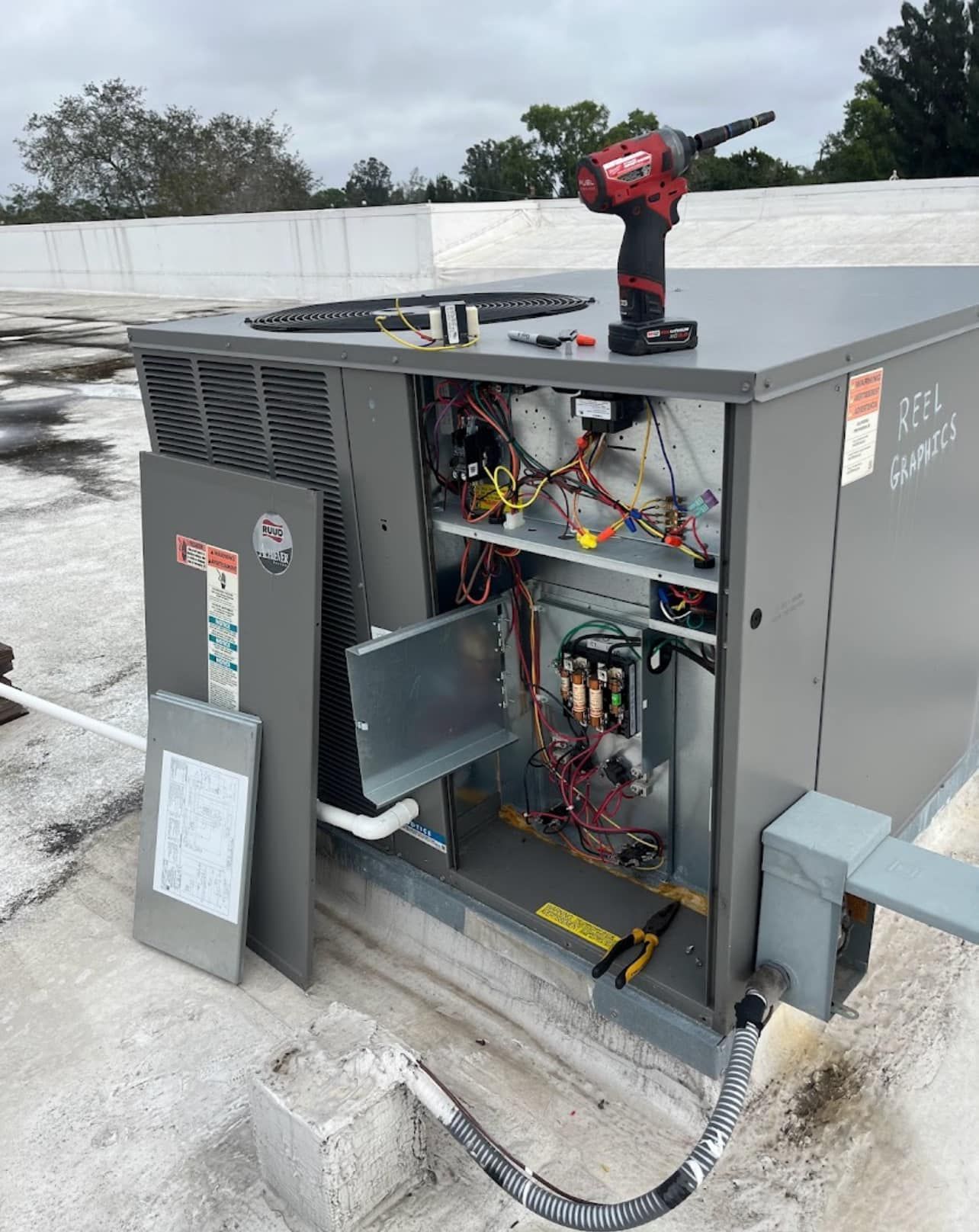 An air conditioner is being repaired on a roof with a drill.