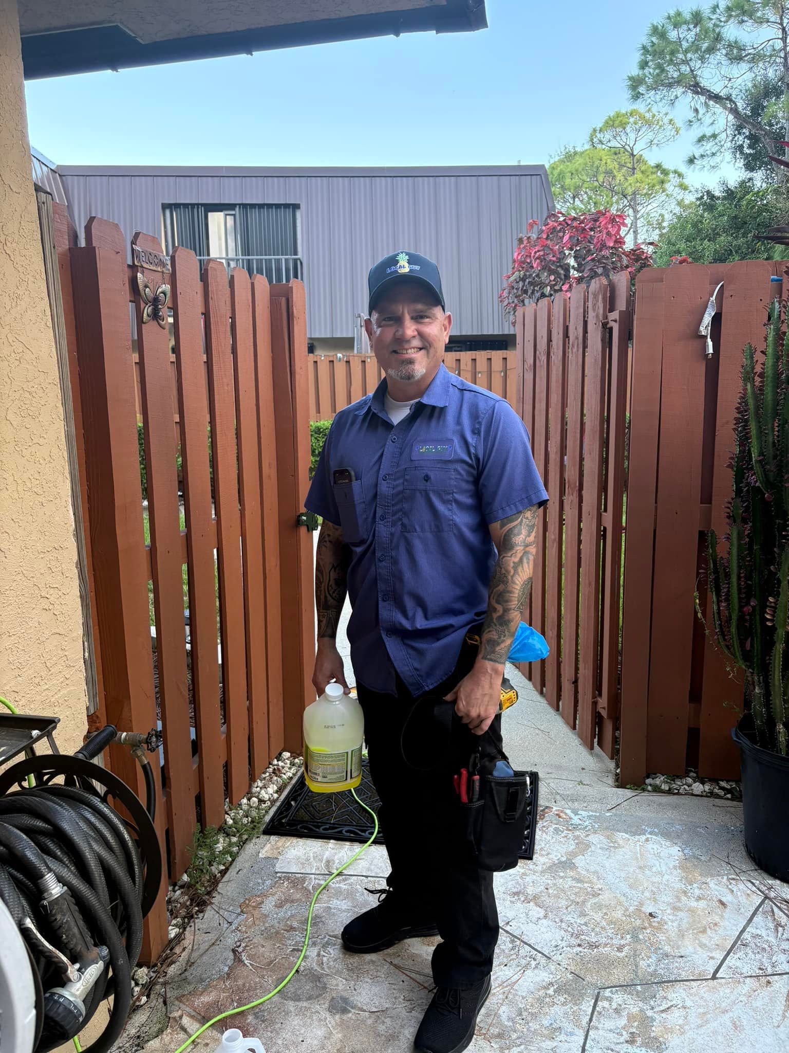 A Local Guy technician in a blue shirt is standing in front of a wooden fence.