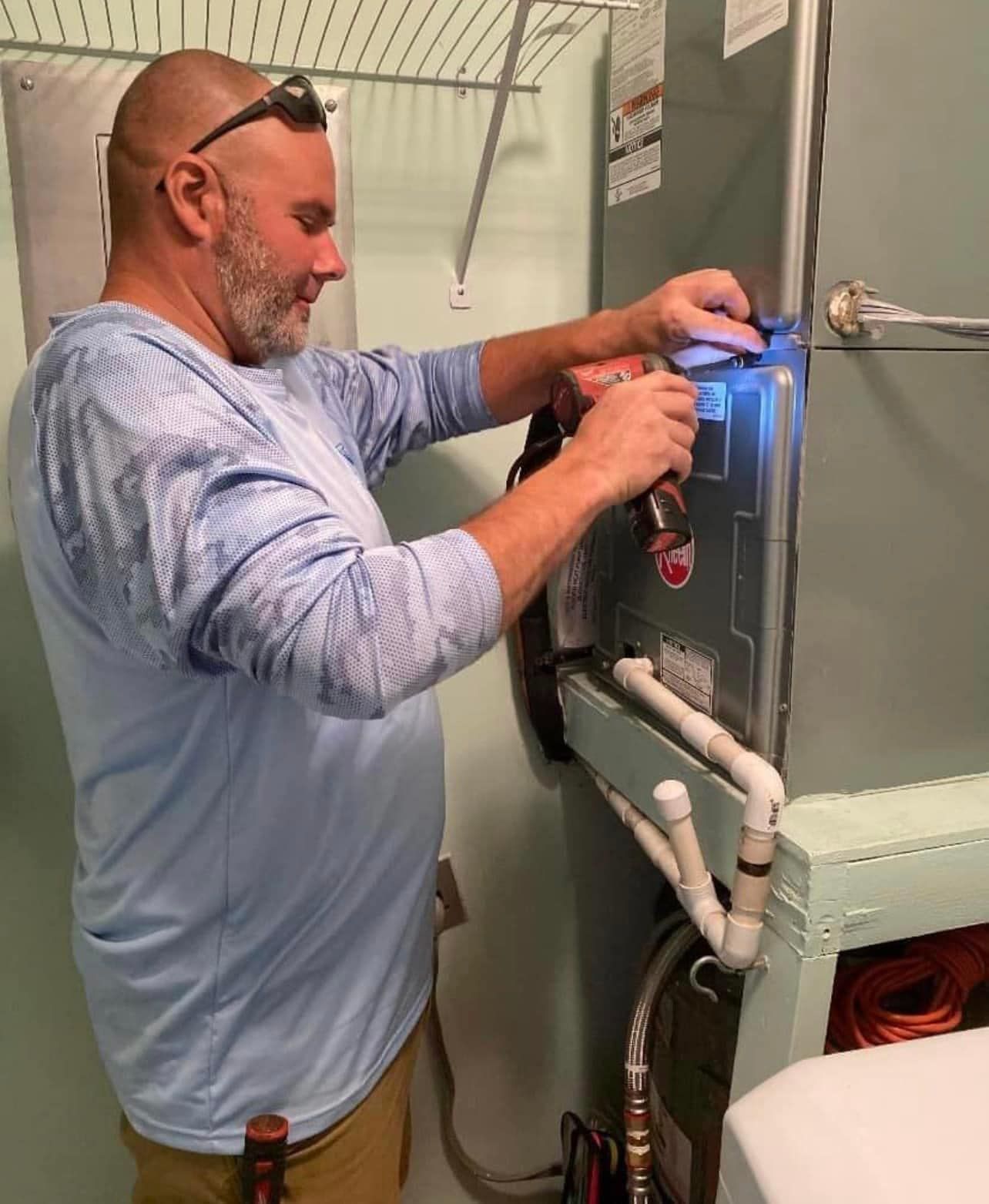 A Local Guy technician is working on an air conditioner in a bathroom.