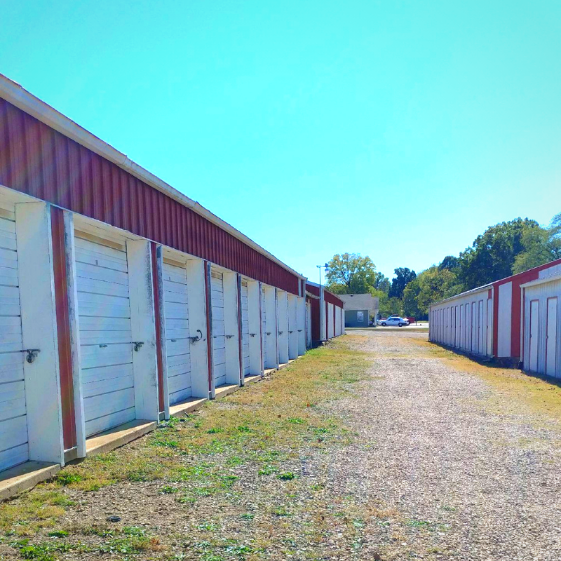 Rows of white storage unit doors lining a gravel lane under a bright blue sky