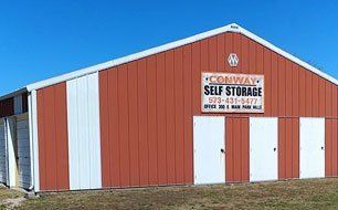 Red self-storage building with white trim and doors under a blue sky, sign reading 