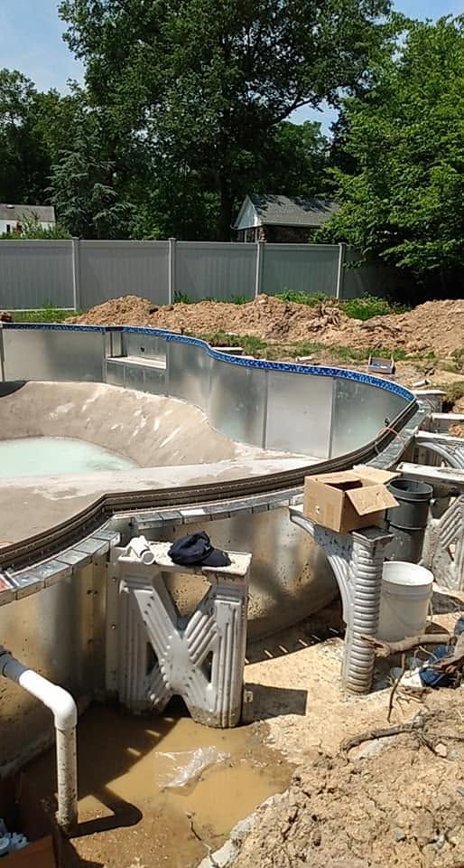 Partially built concrete swimming pool with construction debris and equipment in a muddy backyard