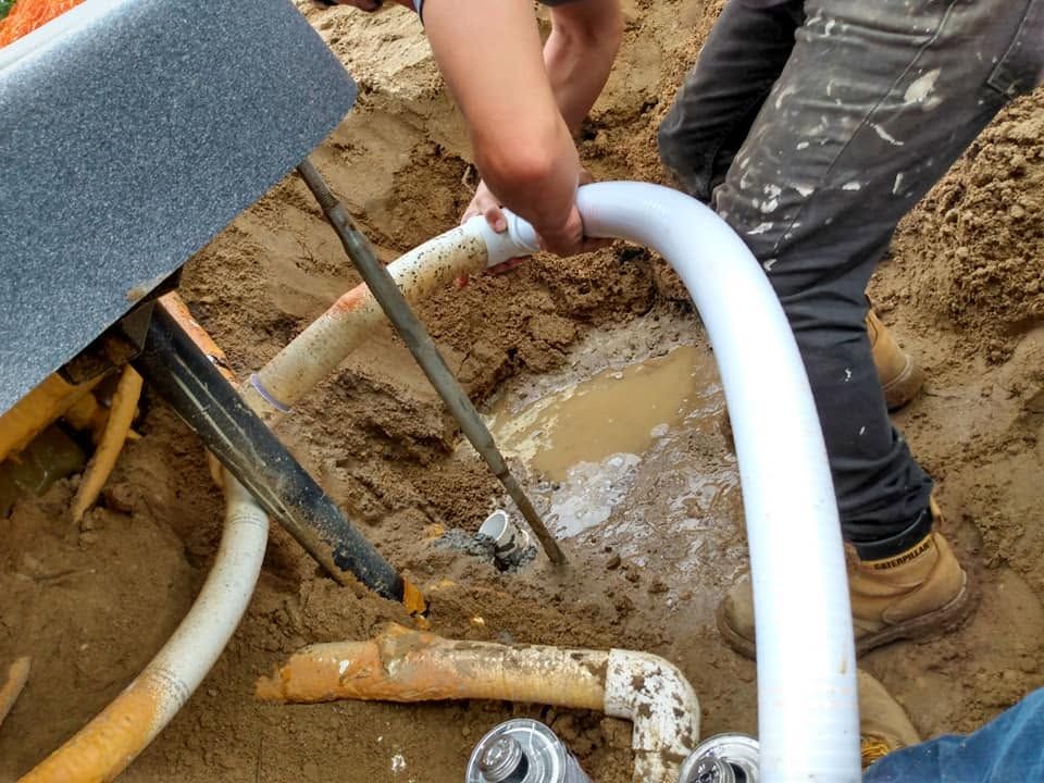Worker connecting white pipe to muddy trench drainage system