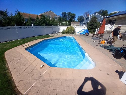 Backyard swimming pool with bright blue water, patio, and a person working near the house