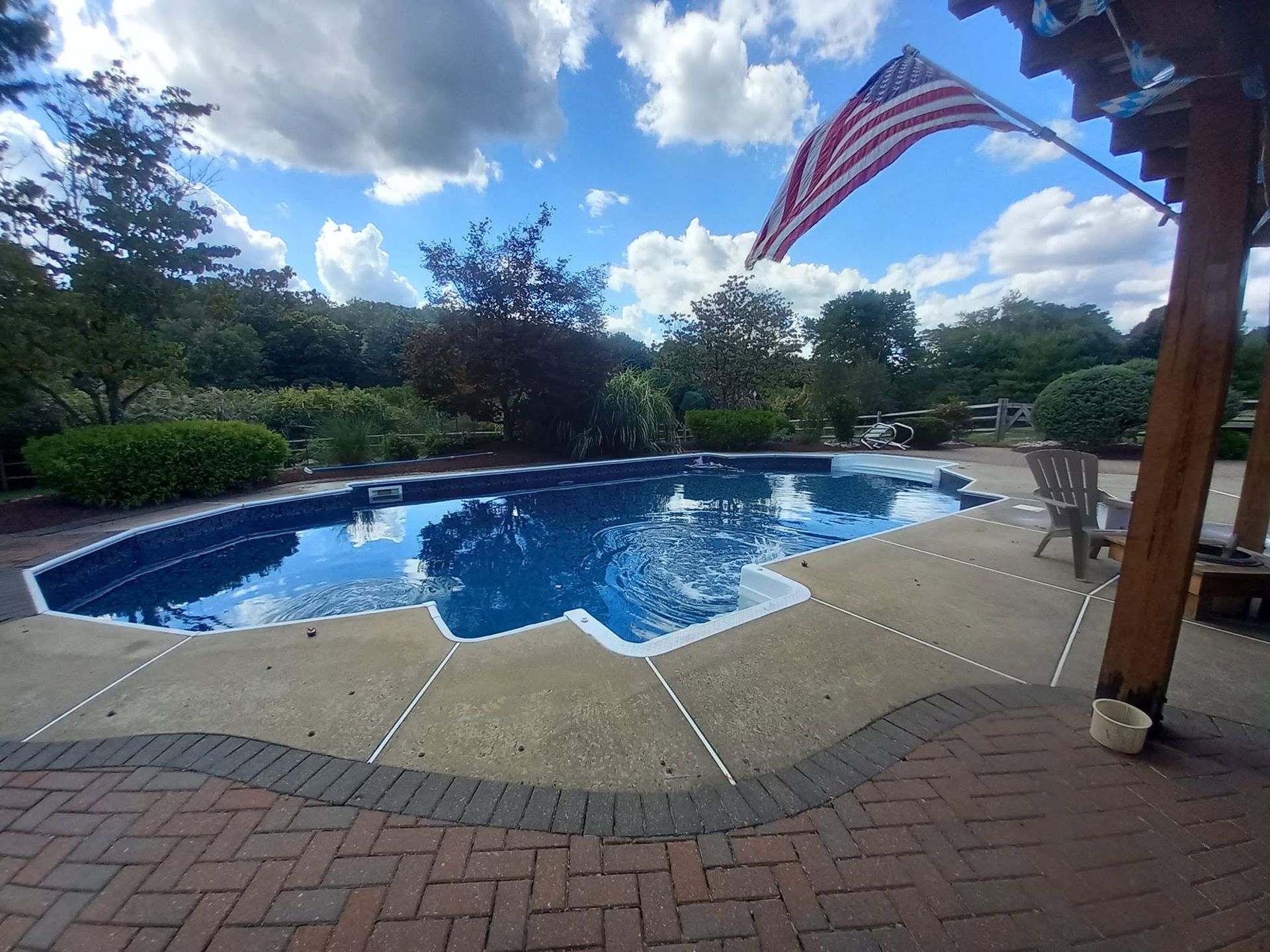 Backyard pool with blue water, patio pavers, trees, and an American flag overhead