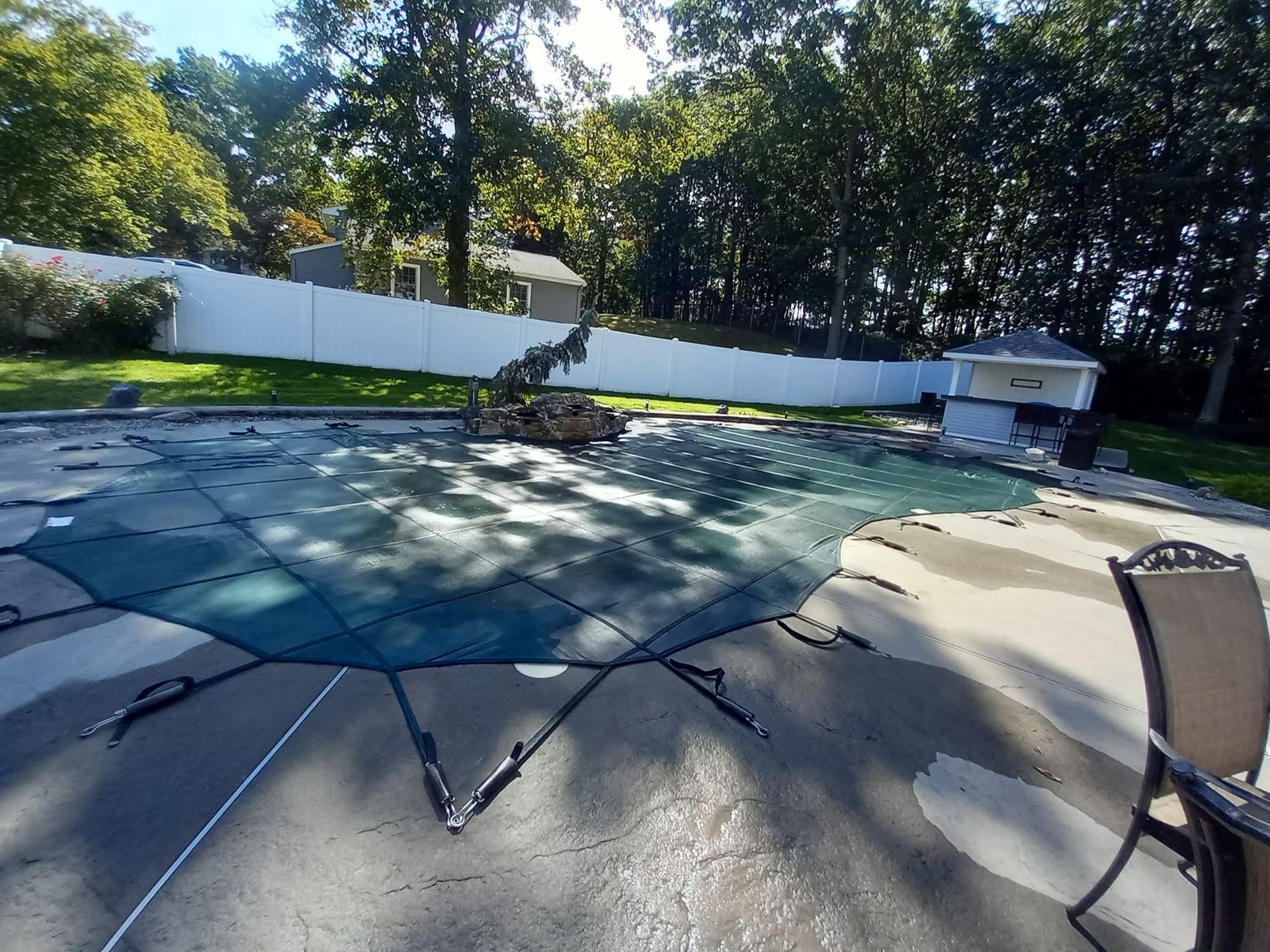 Patio with a covered swimming pool, white fence, and trees in the background