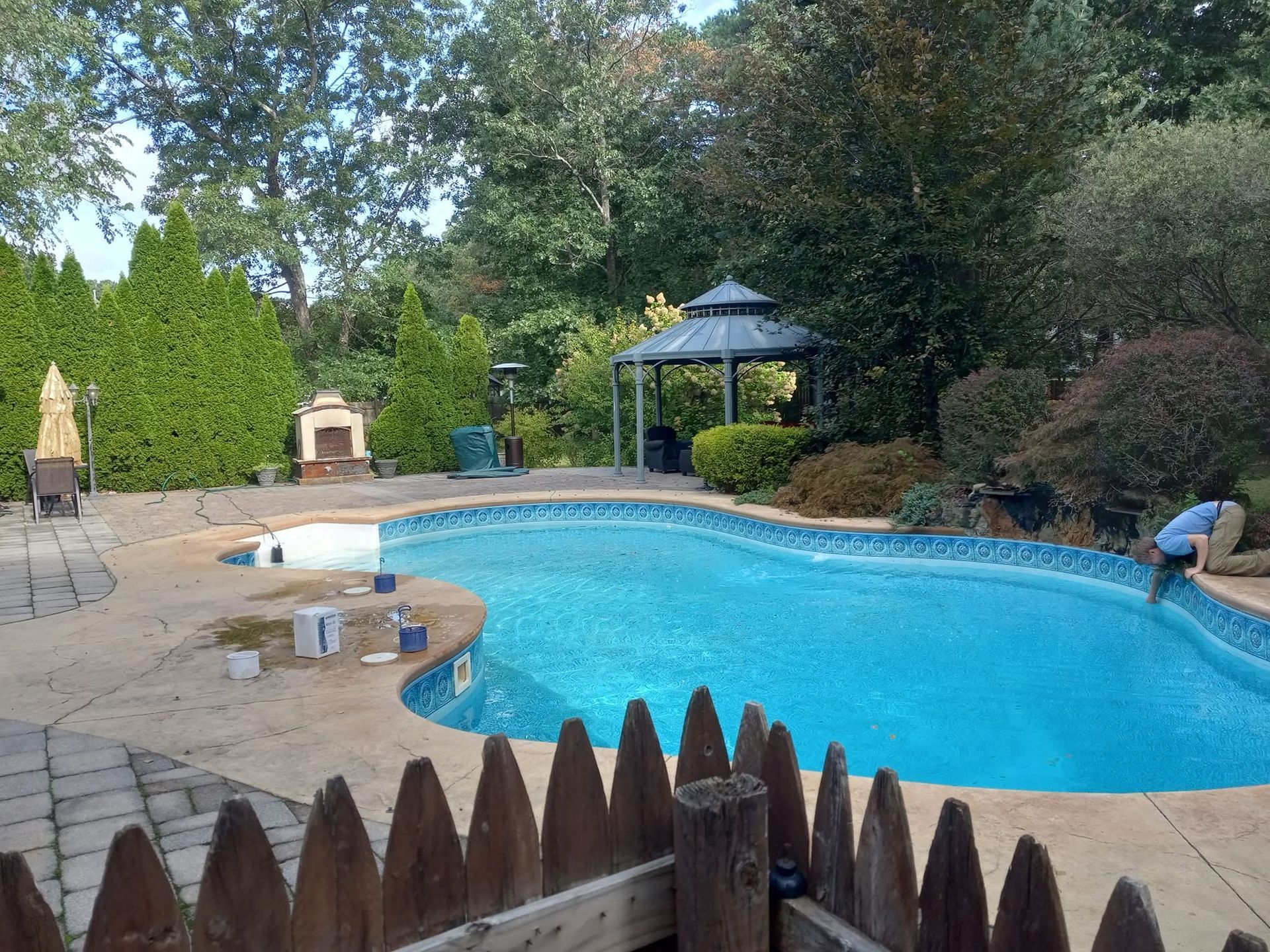 Backyard pool with turquoise water, patio chairs, gazebo, and trees surrounding the deck