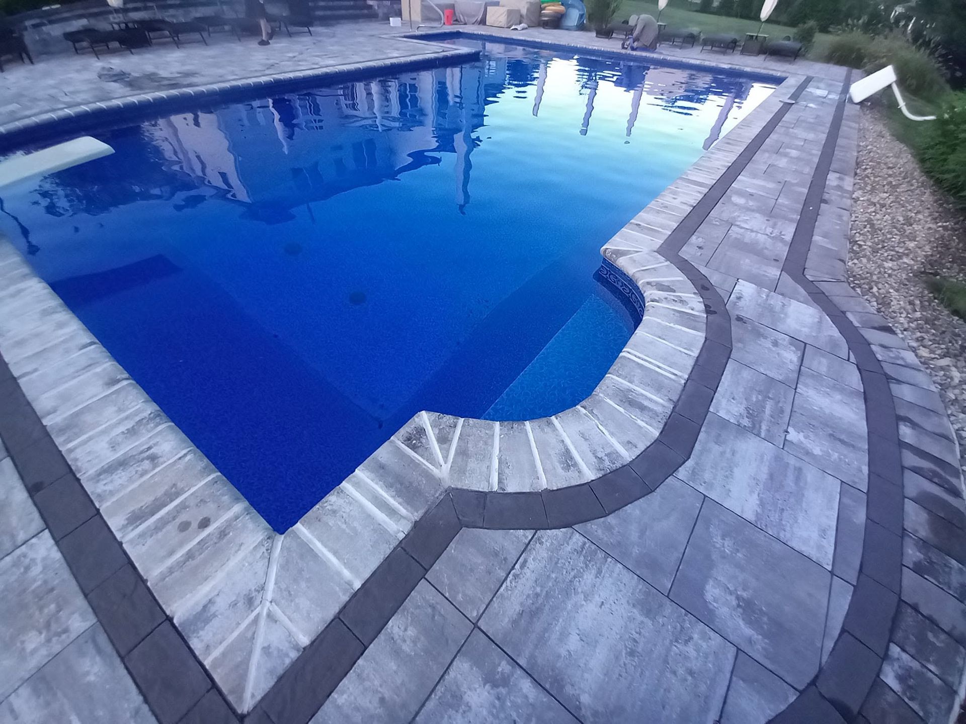 Blue swimming pool with gray stone deck and curved shallow steps along the edge
