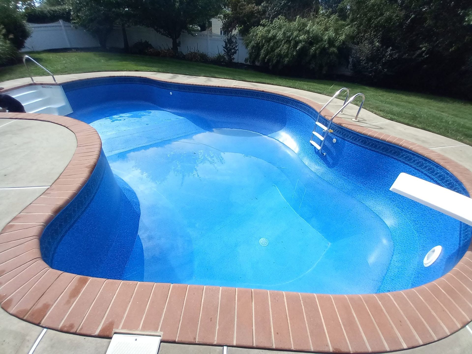 Backyard swimming pool with blue water, brick coping, and a metal handrail