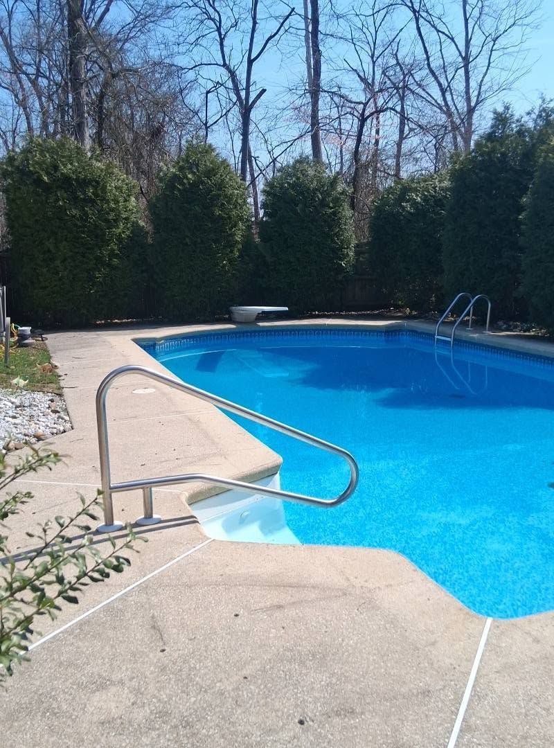 Outdoor swimming pool with blue water, metal handrail, and surrounding trees.