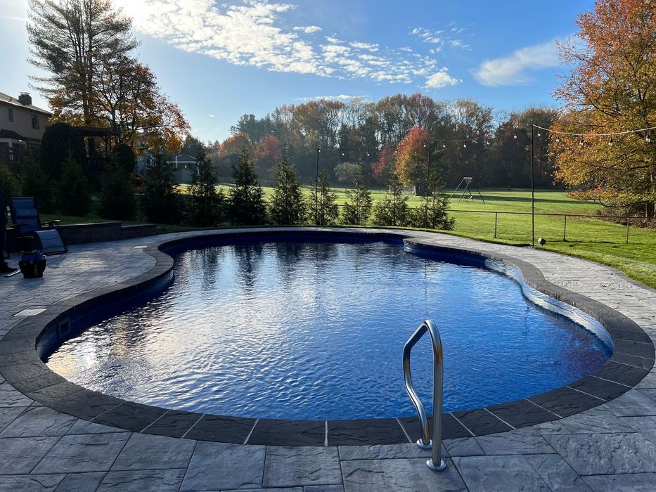 Person spreading a blue tarp over a backyard pool area beside a covered hot tub