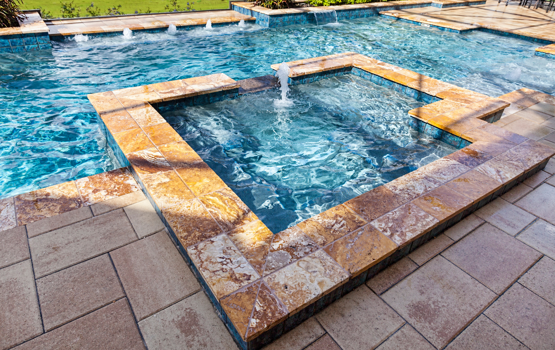 Stone hot tub with bubbling water beside a blue swimming pool and tiled patio