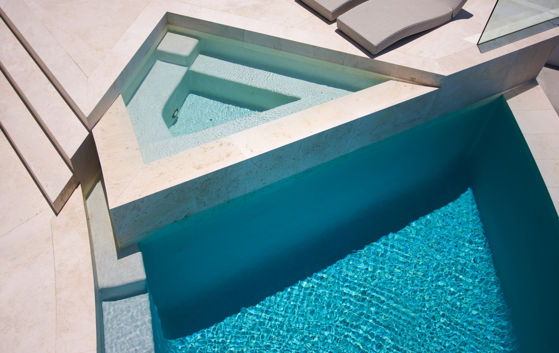 Turquoise swimming pool beside a light stone deck and steps in bright sunlight