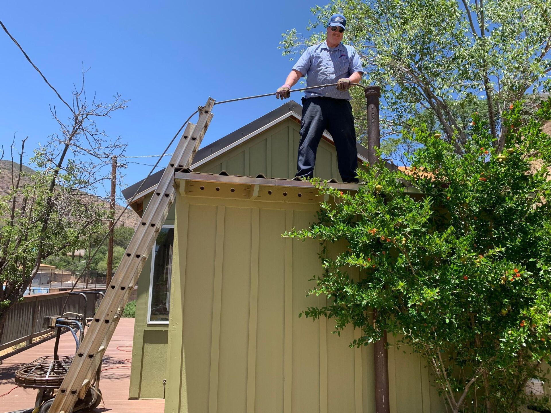A man is standing on the roof of a house with a ladder.