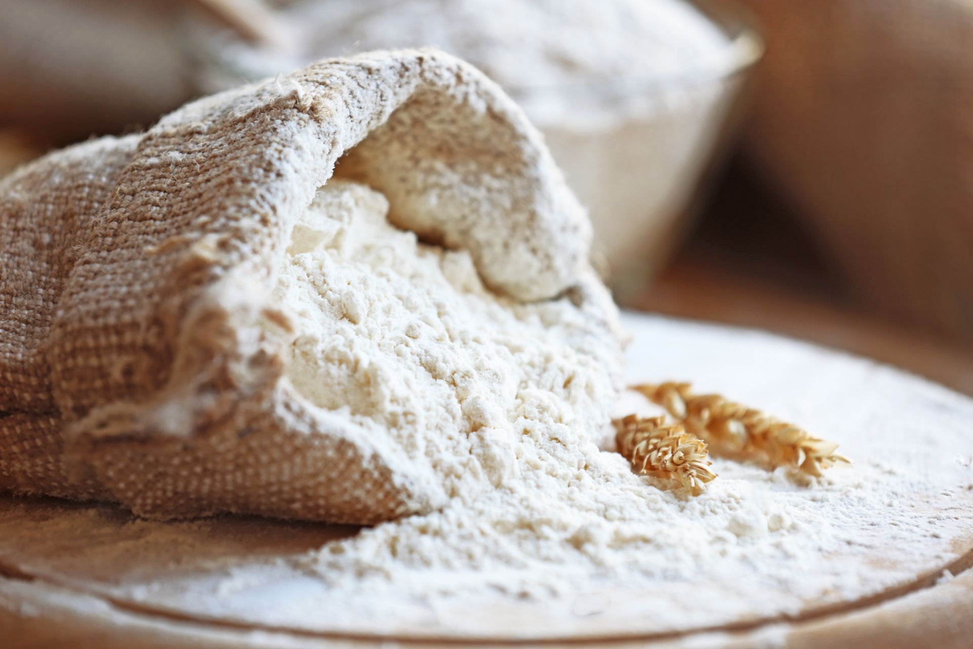 A bag of flour is pouring out of it on a wooden cutting board.