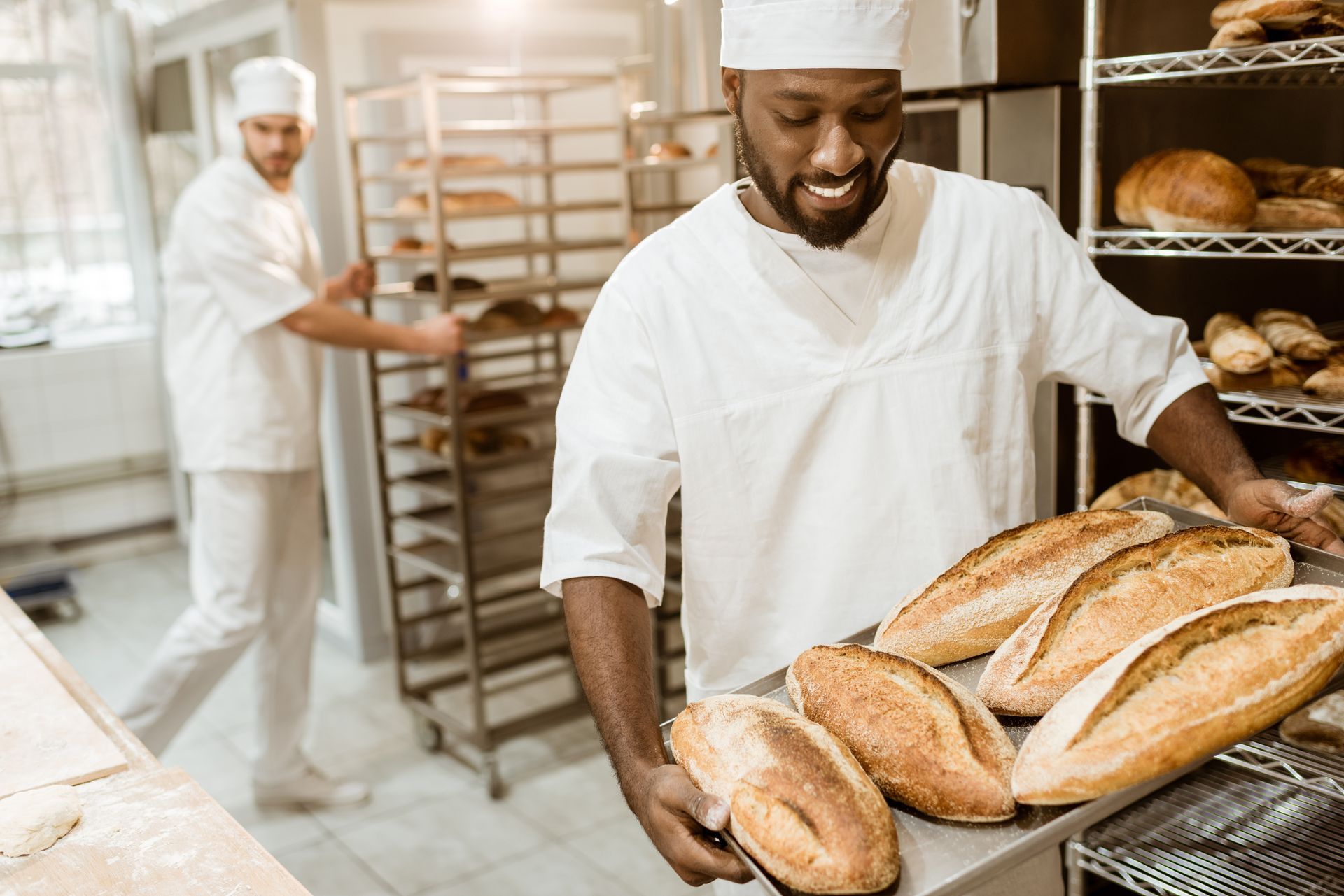 A man is holding a tray of bread in a bakery.