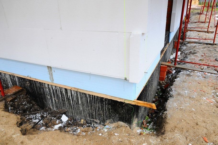 House corner on piers over muddy ground, with orange supports and visible drainage beneath.