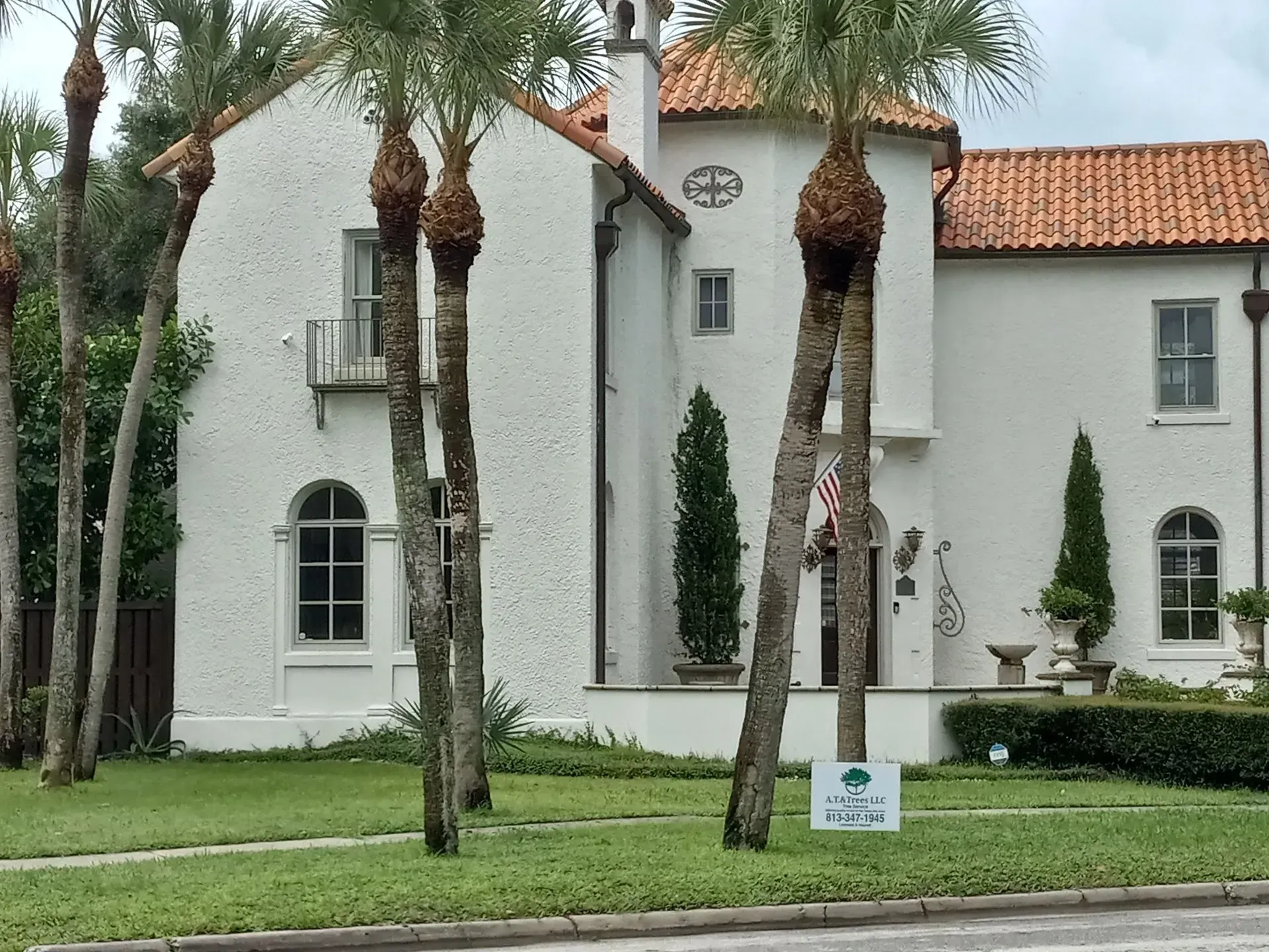 White stucco house with red tile roof and palm trees in a landscaped yard