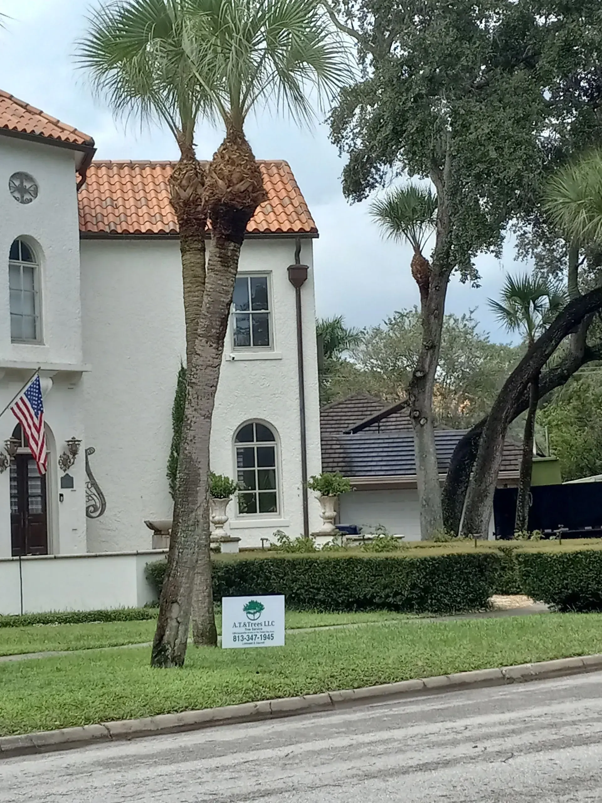 White stucco building with red tile roof, palm trees, and a lawn beside a road