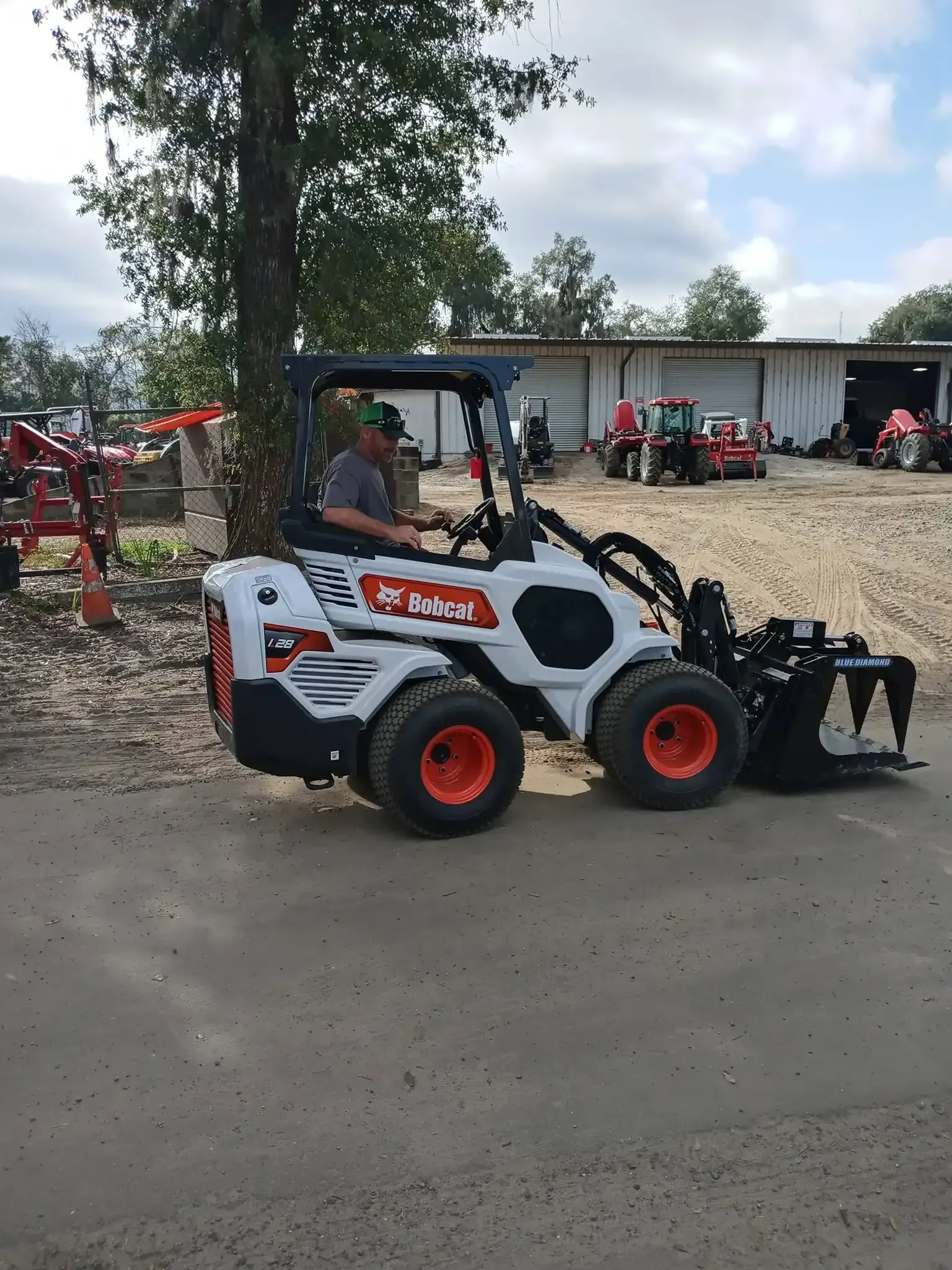 White Bobcat skid steer with red wheels and front attachment on a dirt road near farm buildings