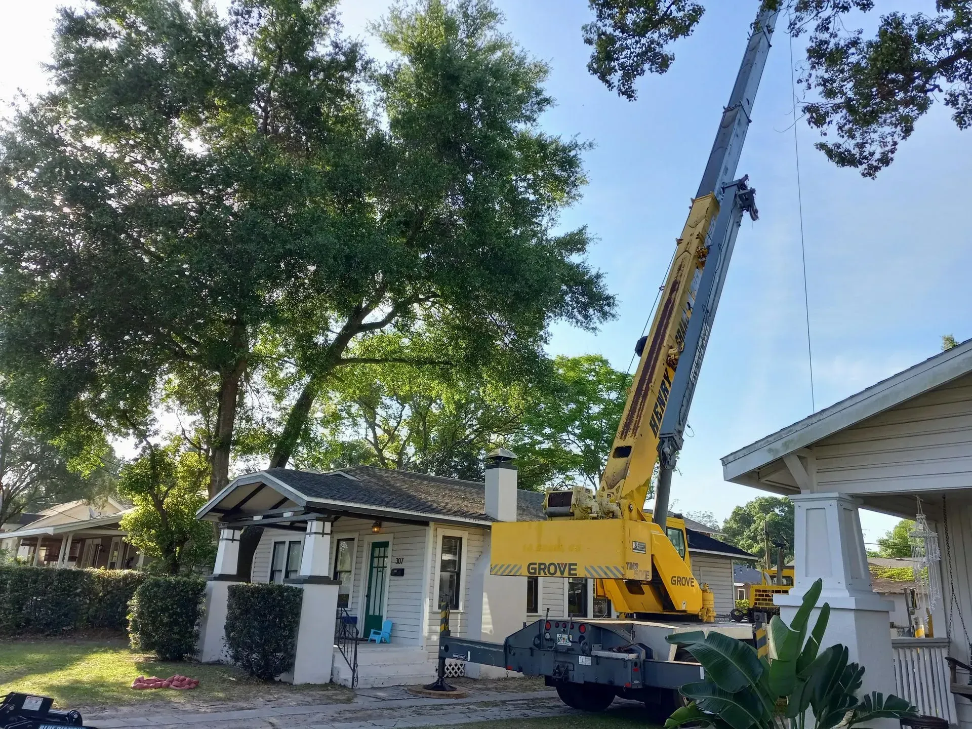 Yellow crane truck lifting a tree in a residential yard beside a white house