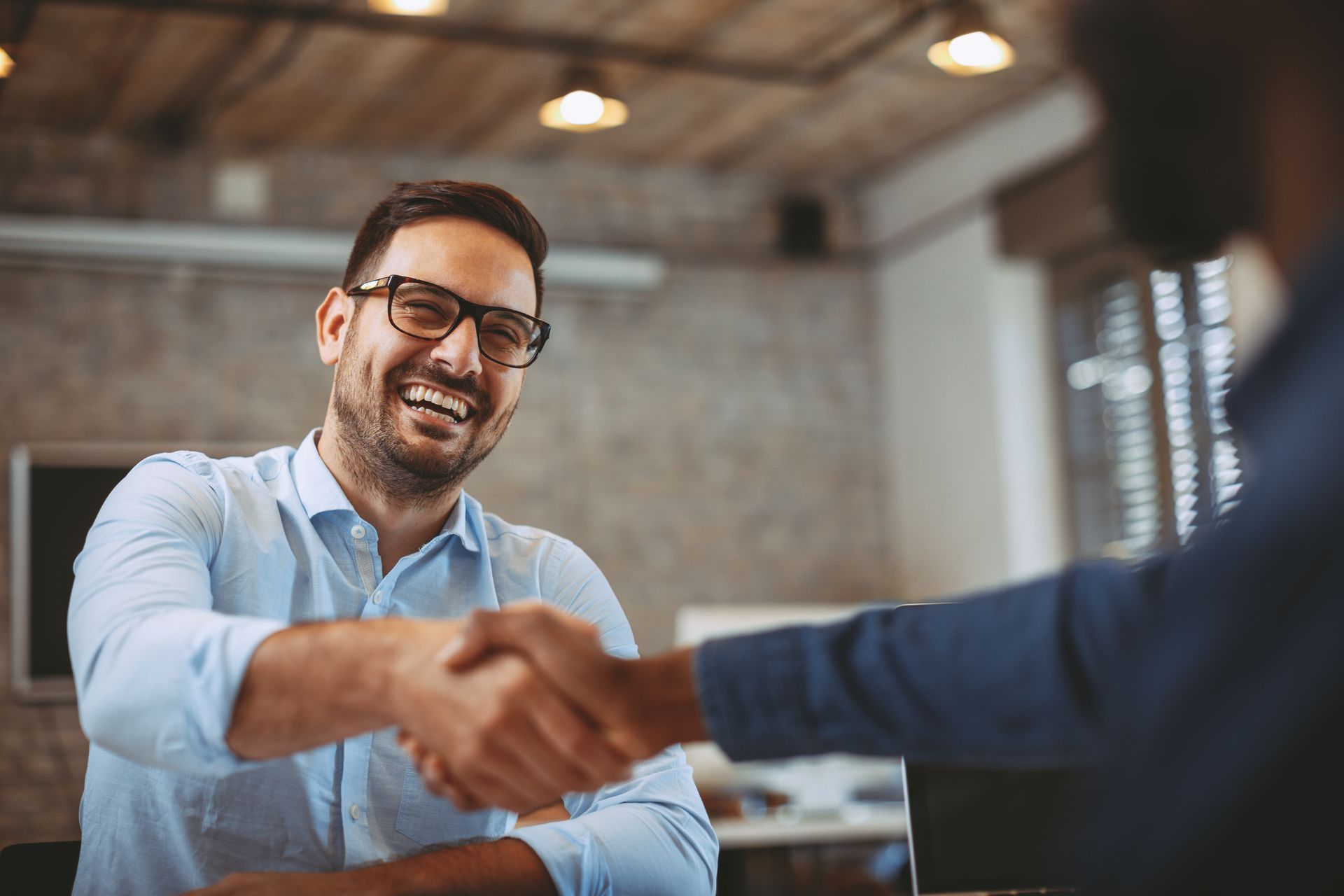 Two people shaking hands in a modern office, with one man smiling in the background.