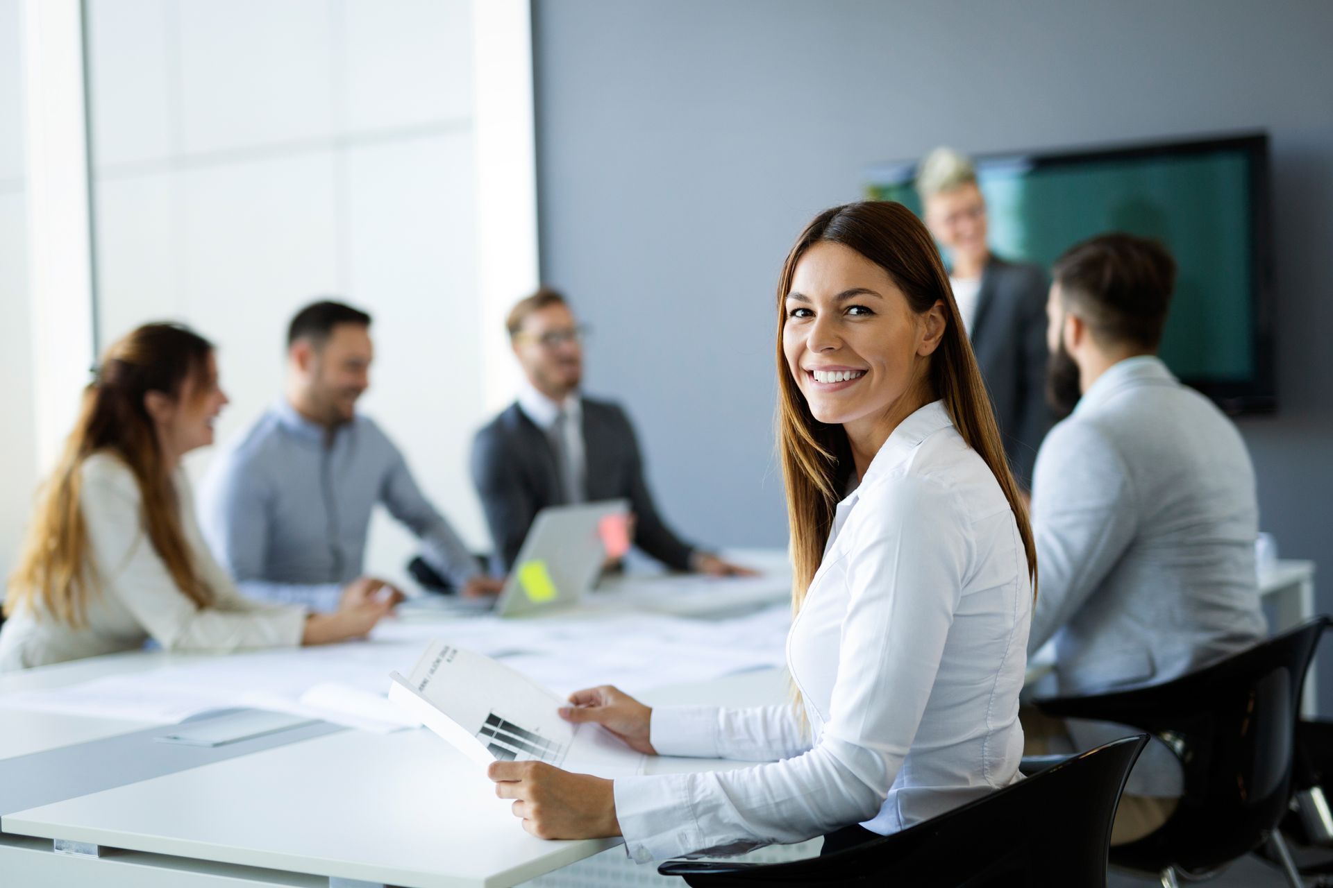 Business meeting in a bright office, with a smiling woman in white at a conference table.