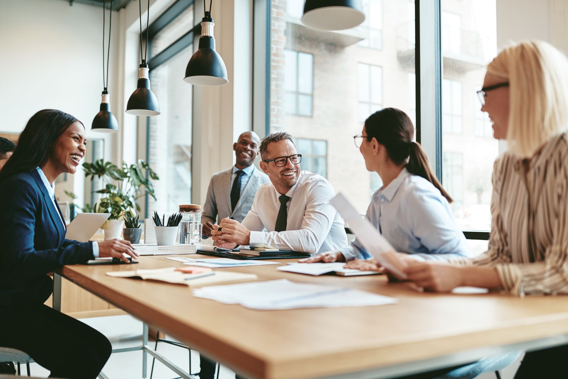 Colleagues in a bright office meeting around a conference table with papers and coffee cups