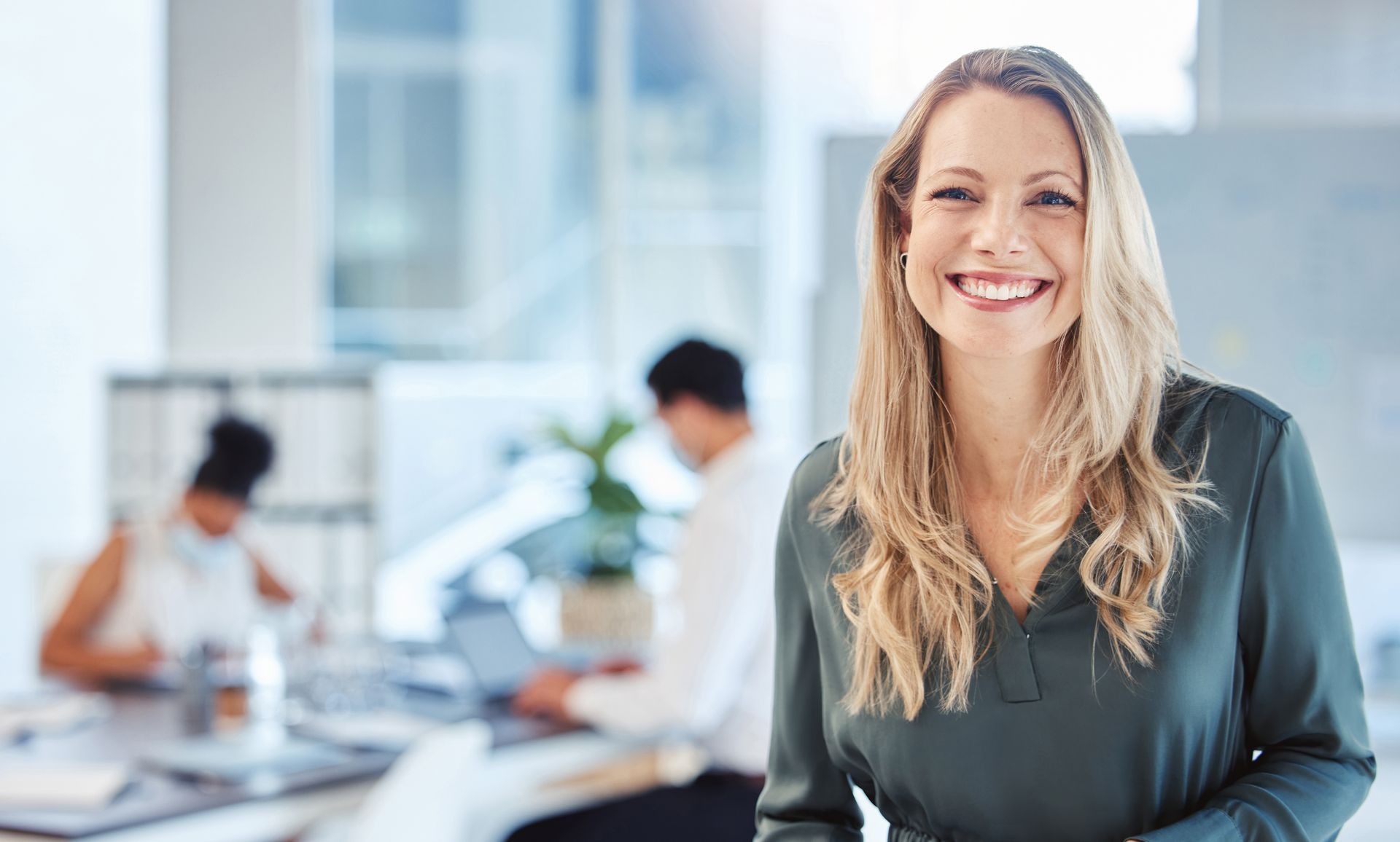 Smiling woman in a bright office with coworkers blurred in the background