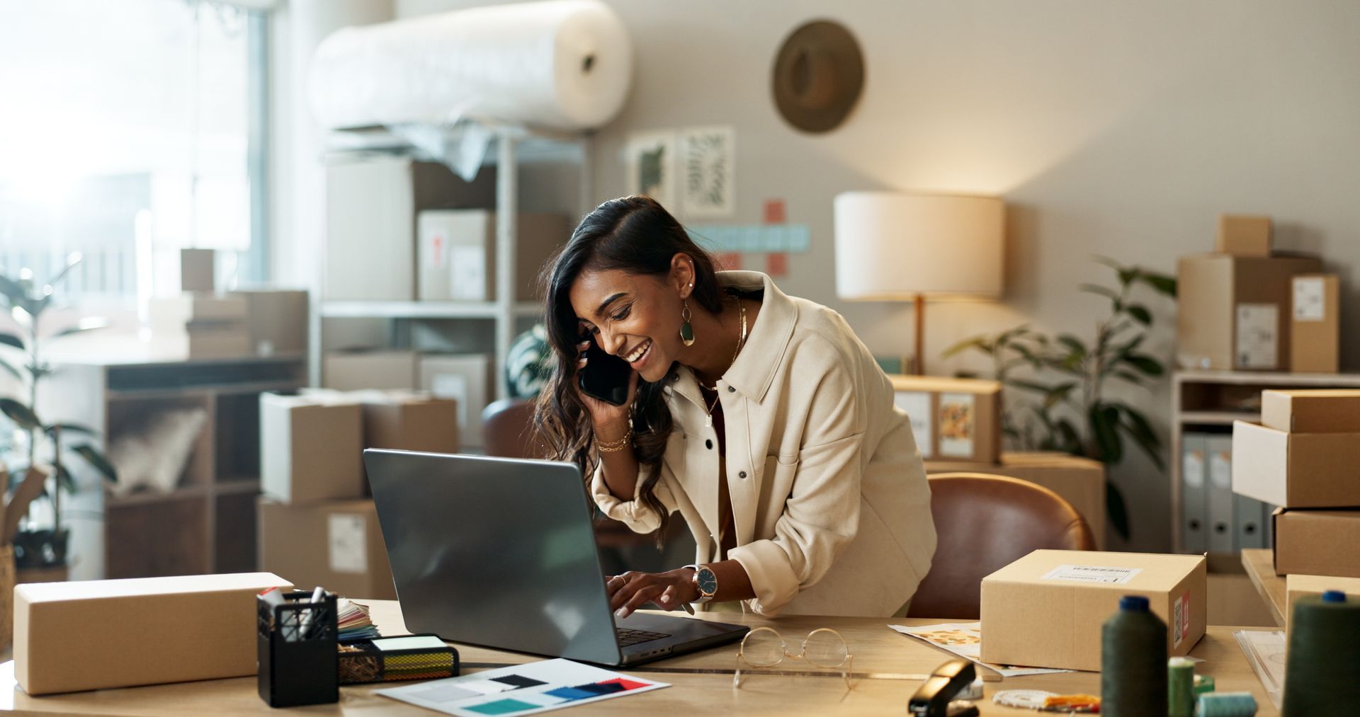 Person working on a laptop at a desk in a cozy home office, surrounded by papers and plants.