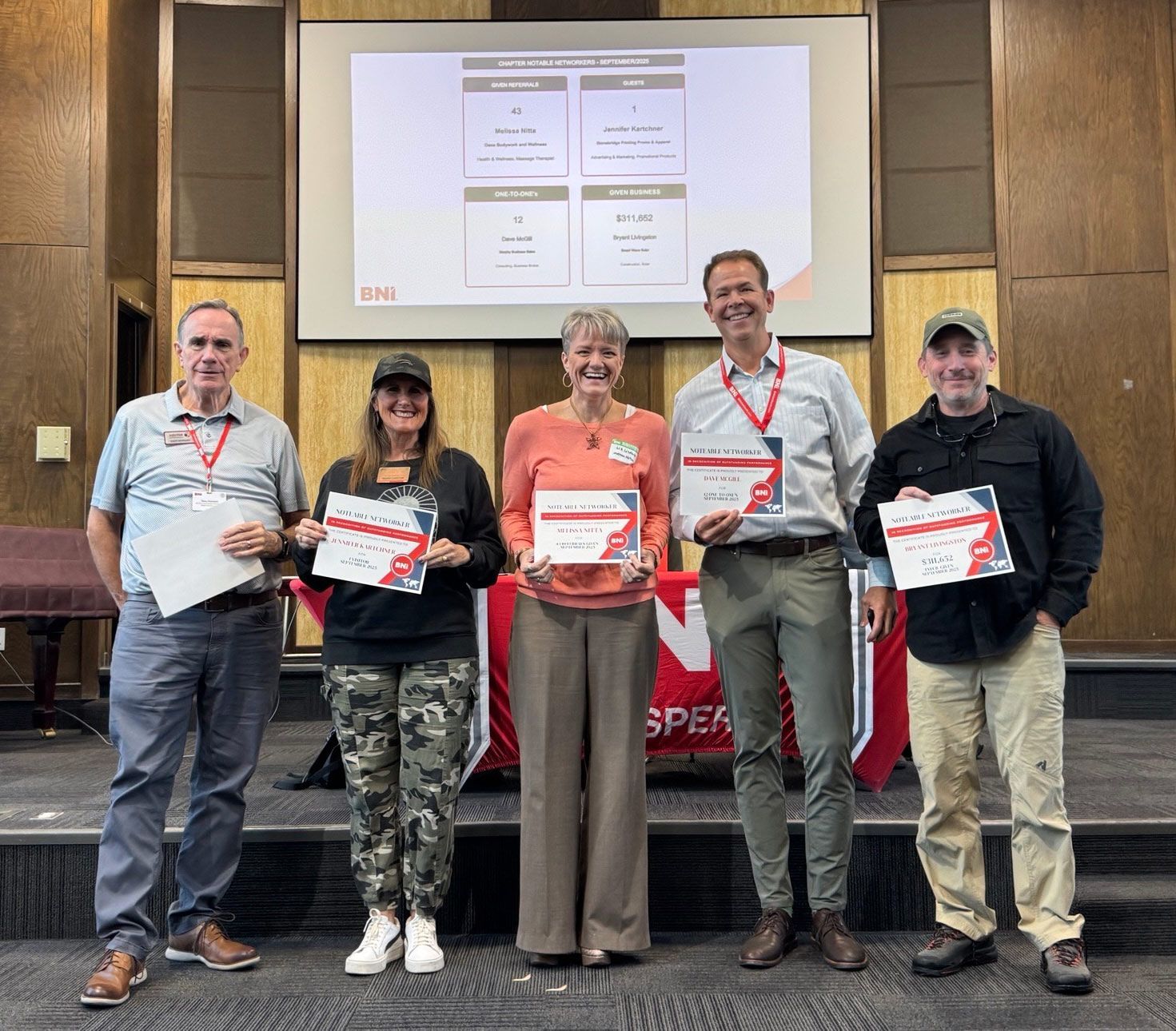 Five people on stage holding certificates at an awards ceremony, with a presentation screen behind them.