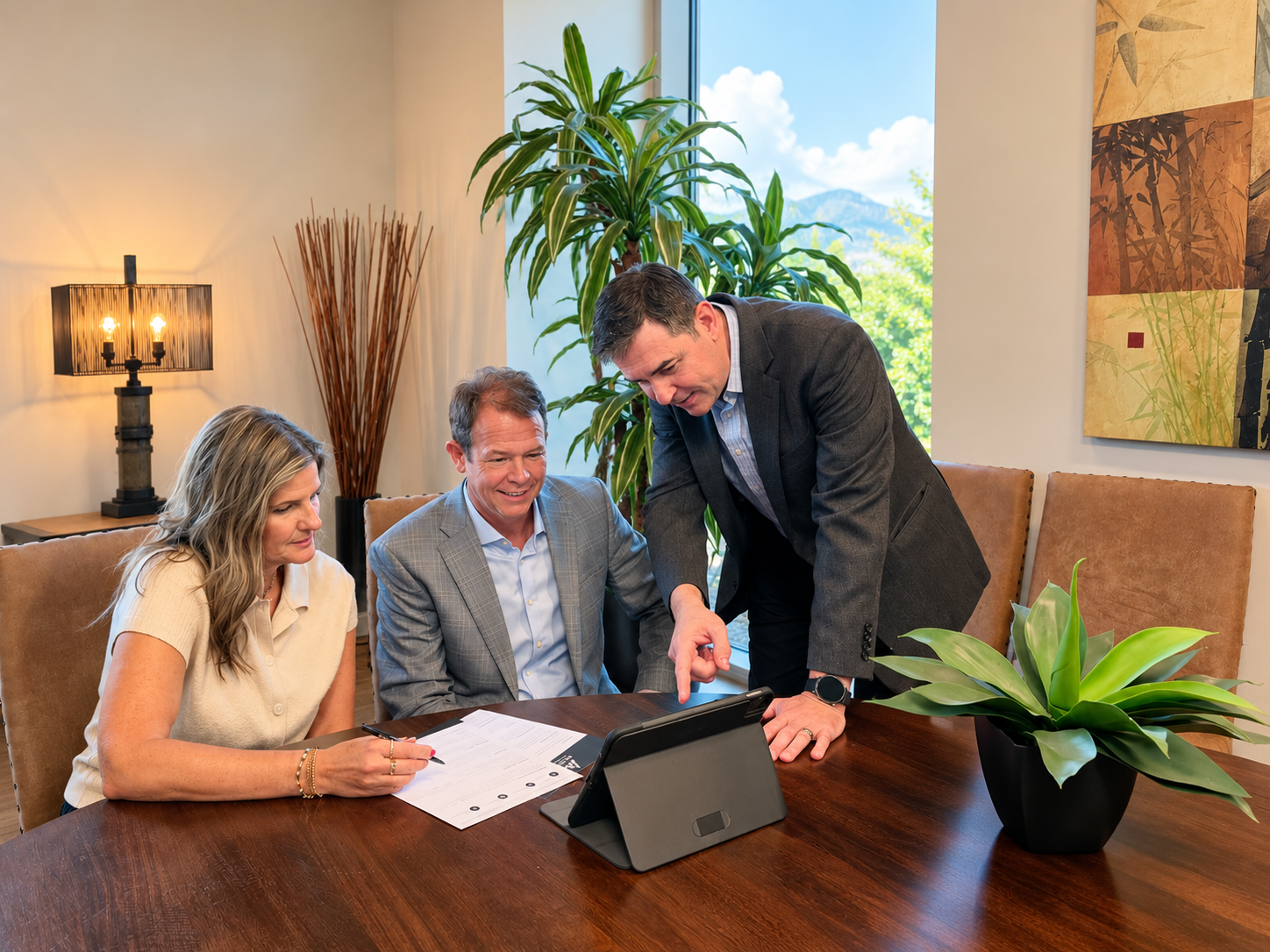 Three people review documents on a tablet at a conference table in an office setting.