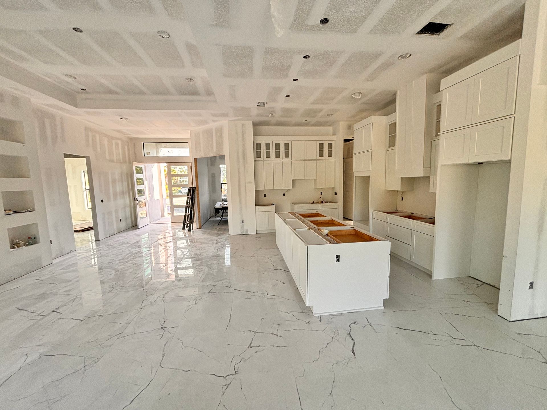 Bright unfinished kitchen with white cabinets, marble floor, and center island under construction