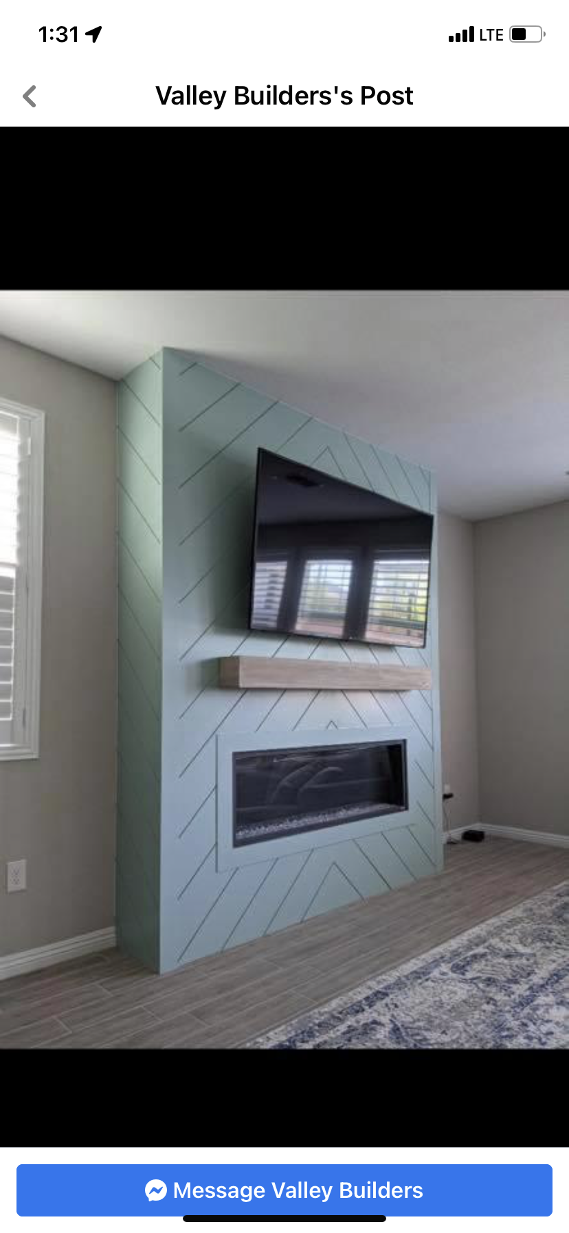 Modern living room with a gray tiled fireplace and mounted TV above it, next to a window and carpeted floor.