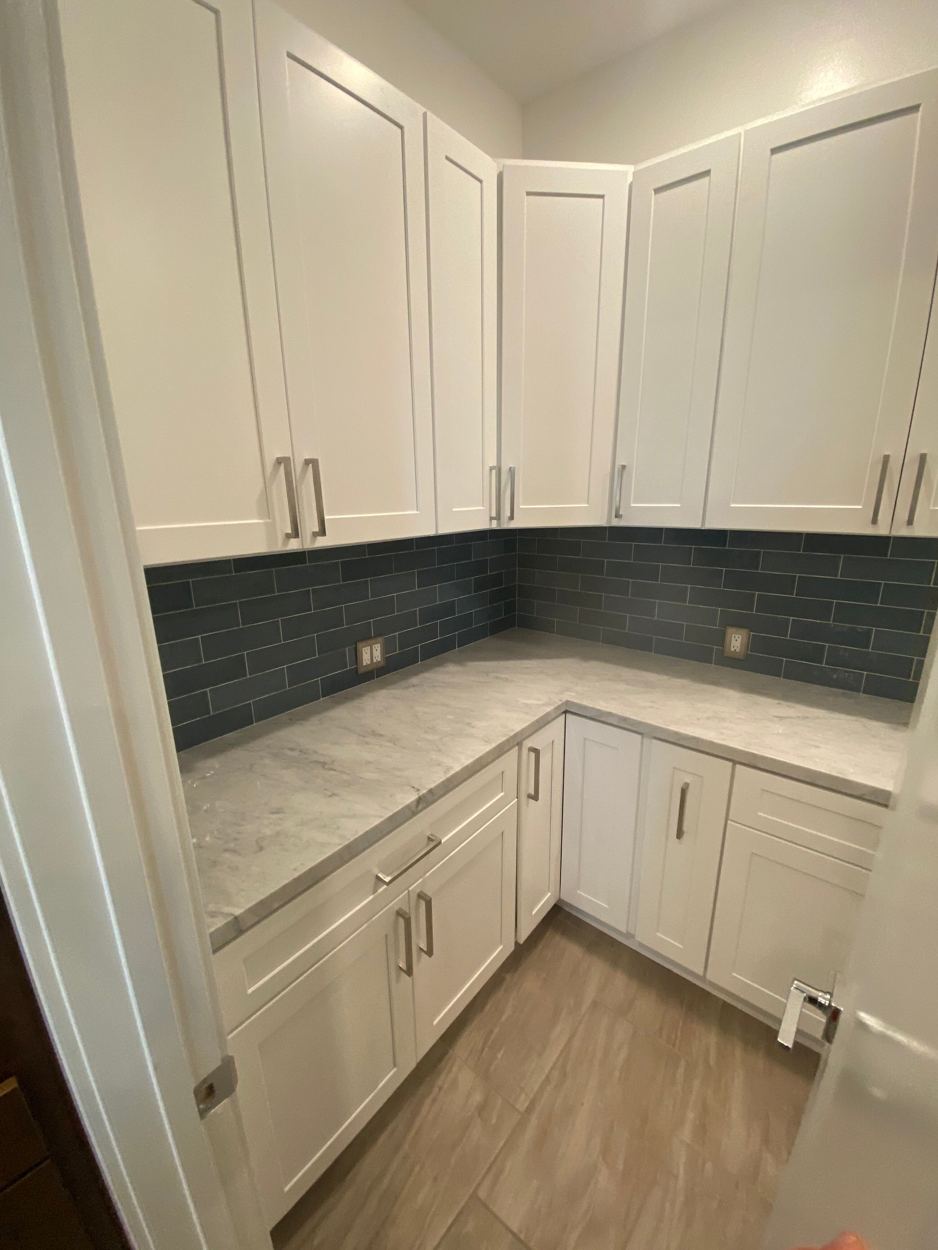 Small white kitchen with dark tiled backsplash, light countertops, and wood floor.