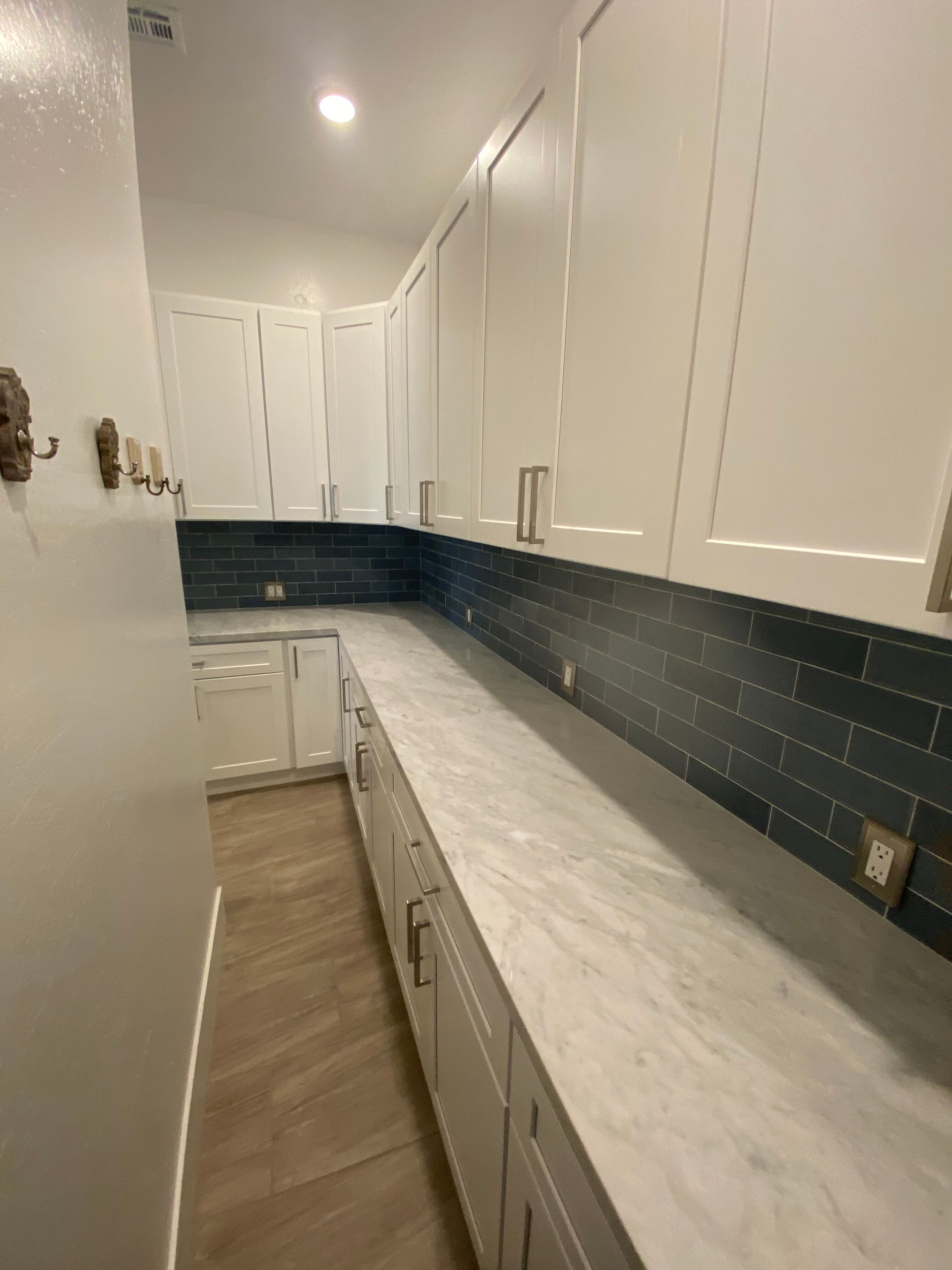 Narrow kitchen with white cabinets, dark tile backsplash, and a long light countertop