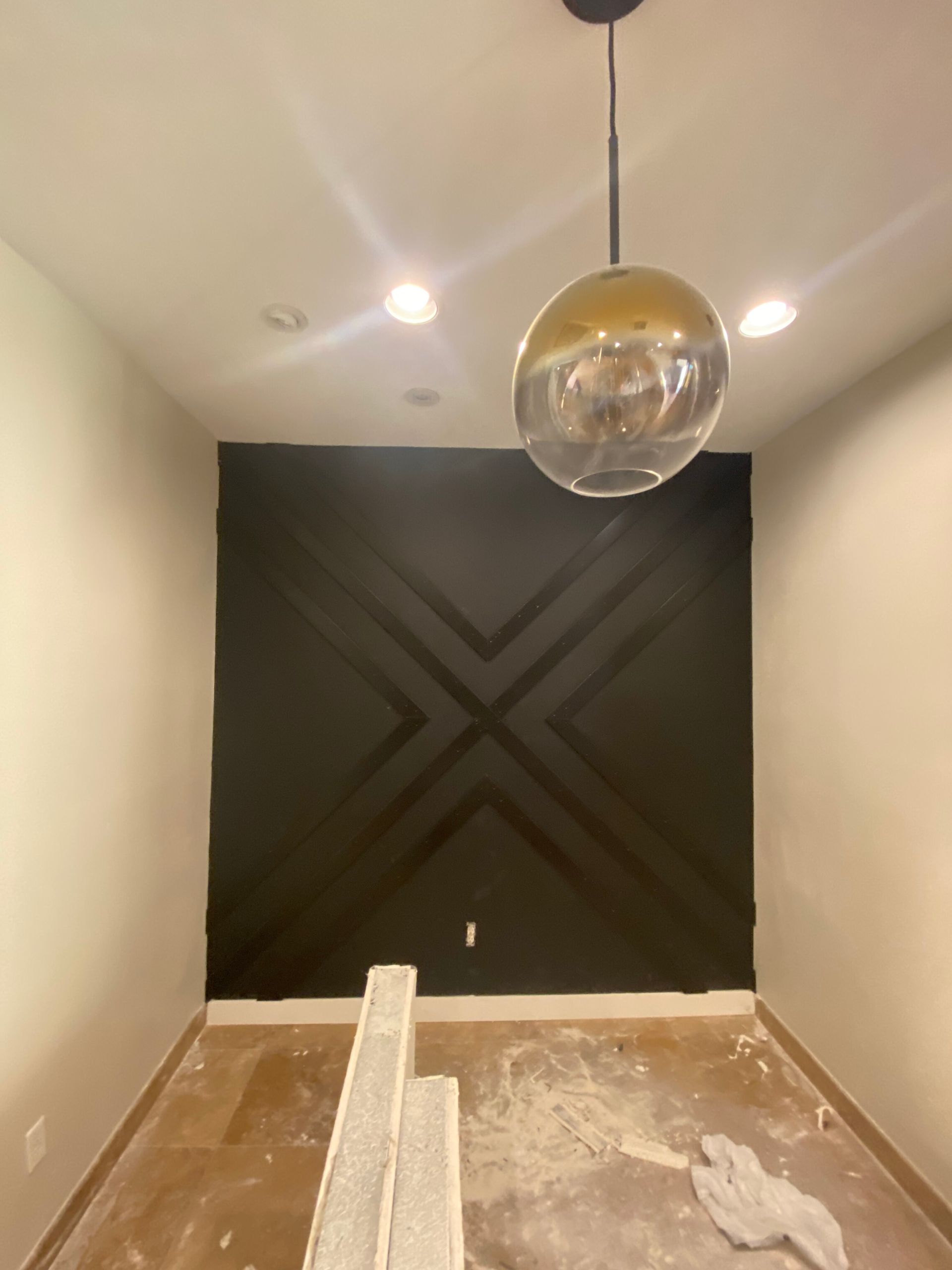 Empty modern room with black accent wall, beige walls, and a hanging globe pendant light.