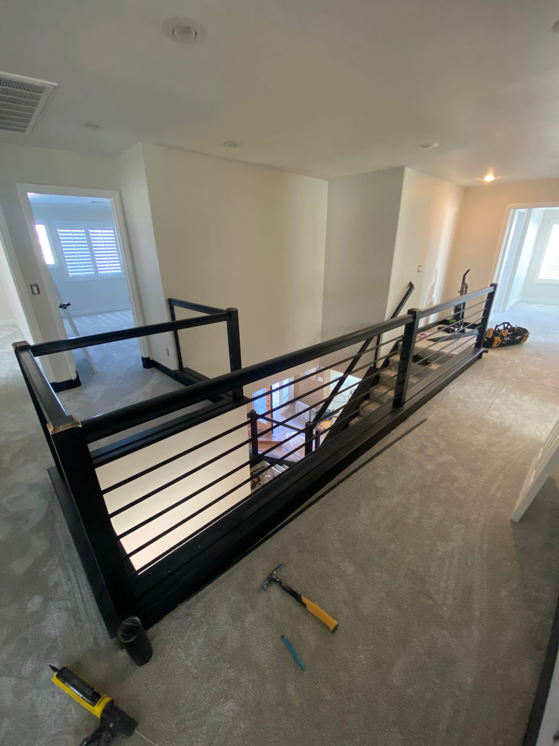 Interior hallway with a black railing around an open stairwell and tools on the carpeted floor.