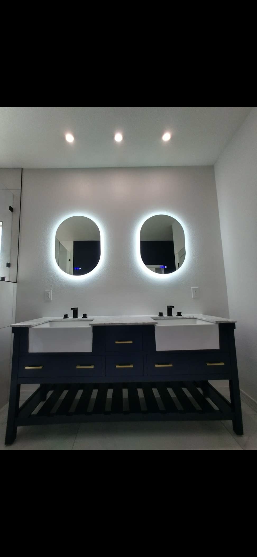 Modern bathroom vanity with two oval mirrors, dual sinks, and dark cabinets under bright ceiling lights