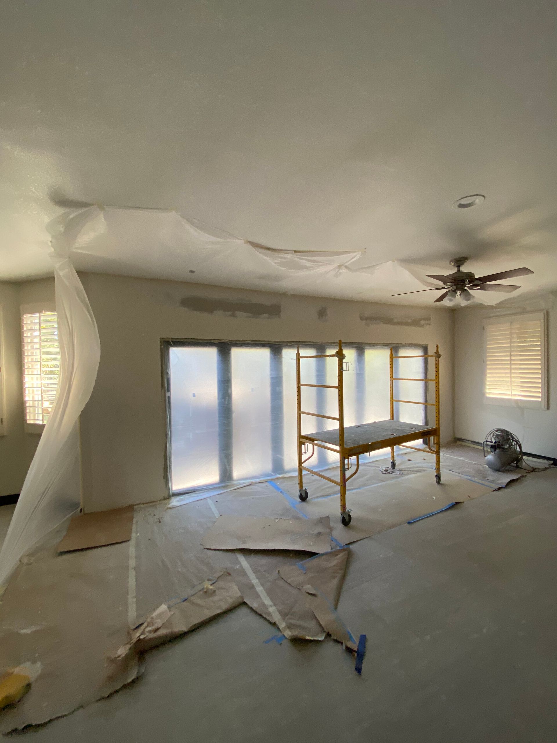 Living room under renovation with scaffolding, torn drywall, and ceiling damage