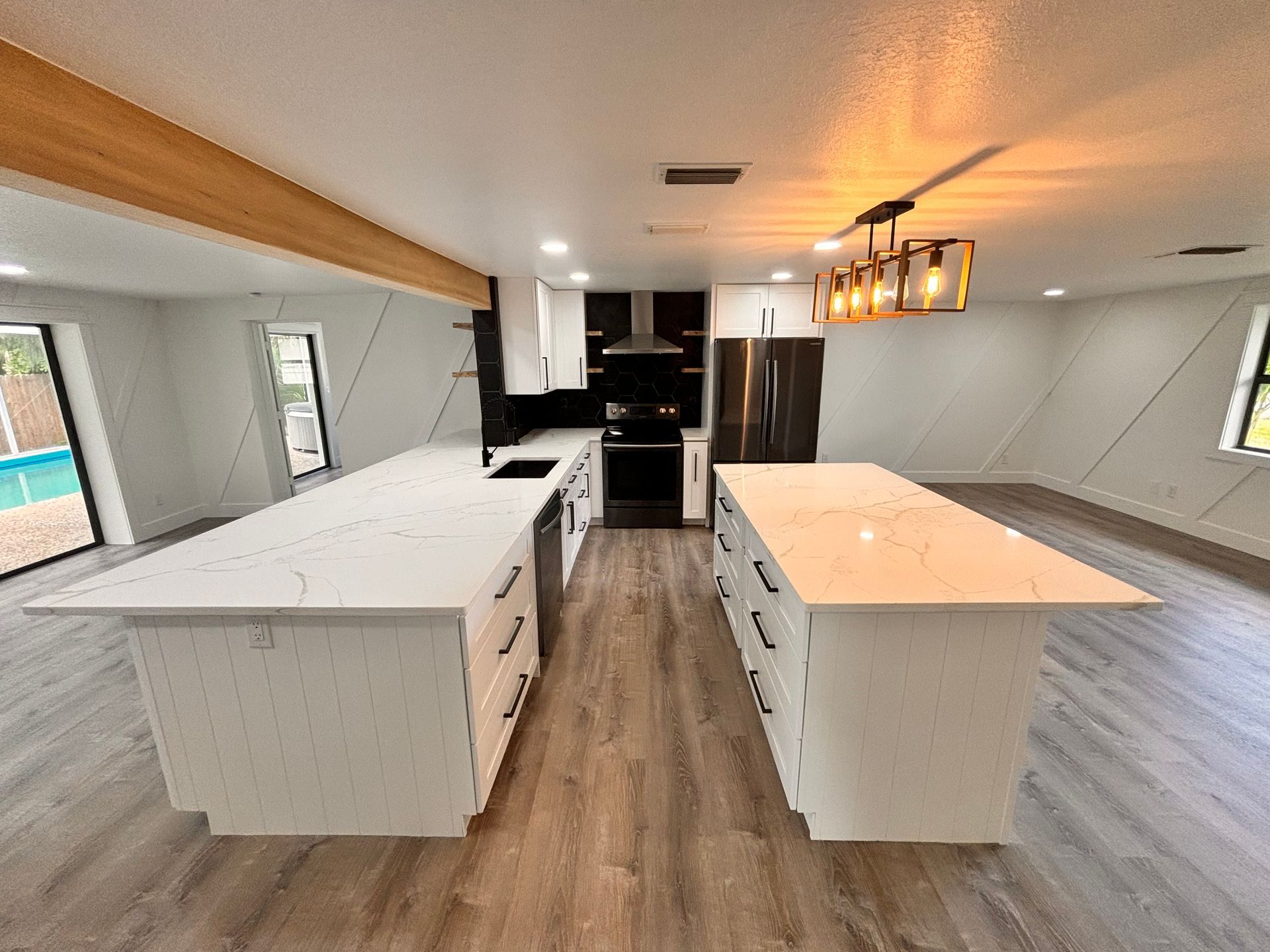 Bright modern kitchen with two white islands, wood floors, dark cabinets, and pendant lights