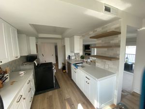 Bright kitchen under renovation with white cabinets, wood floors, open shelves, and a black stove.