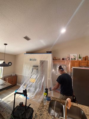 Person unpacking in a kitchen-dining room with furniture wrapped in plastic