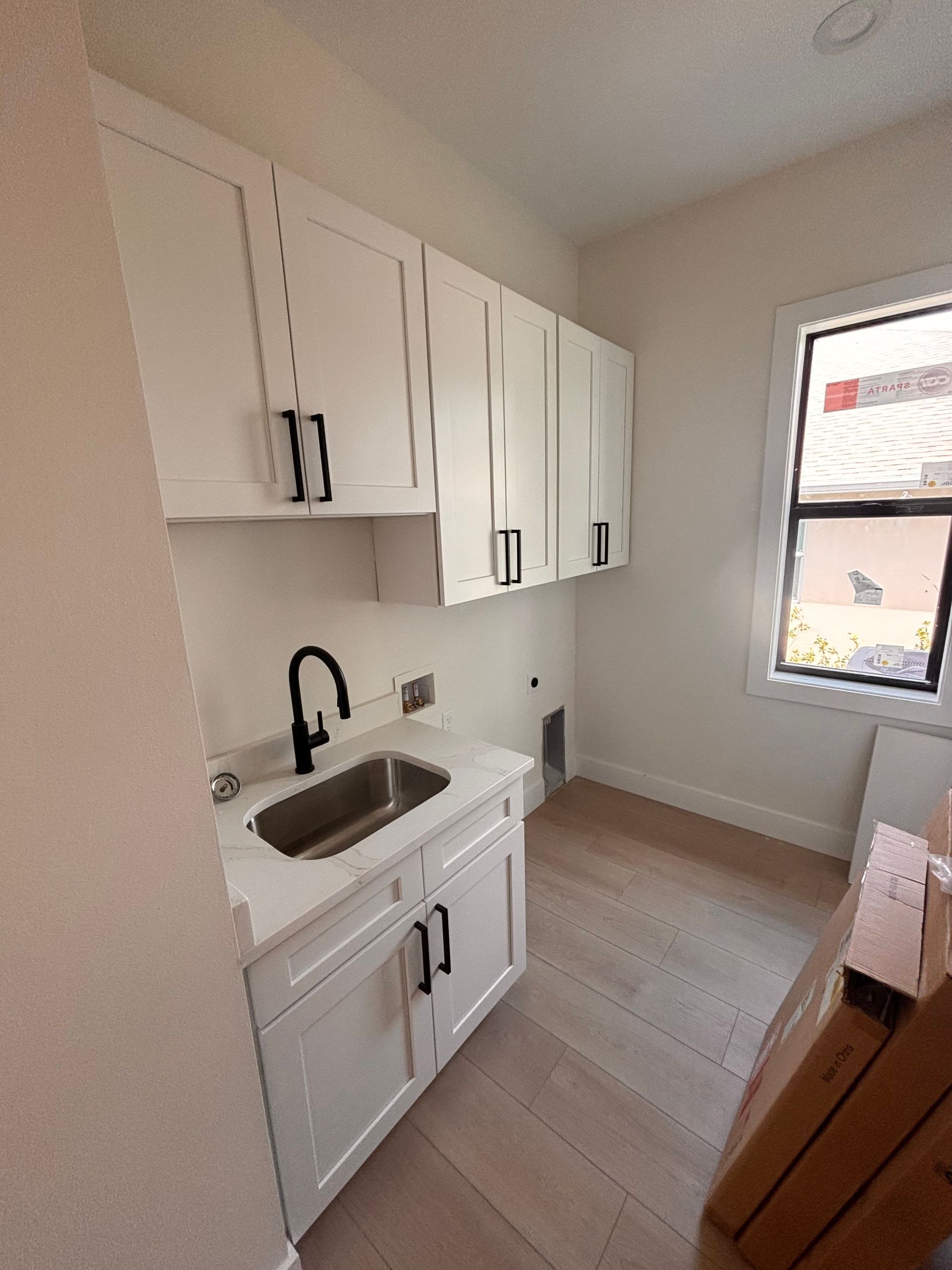 Compact white kitchen with cabinets, sink, stove, and a window in a bright room