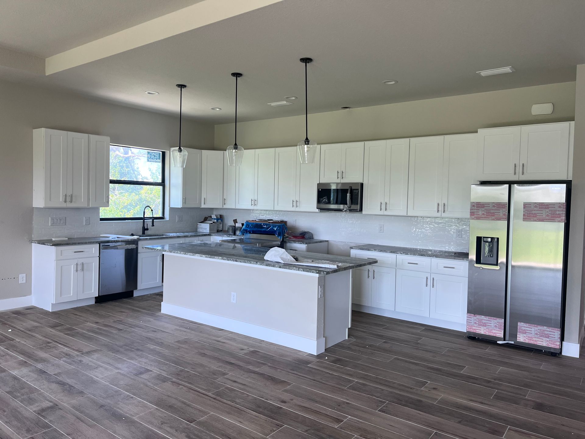 Bright modern kitchen with white cabinets, island, stainless appliances, and wood-look flooring
